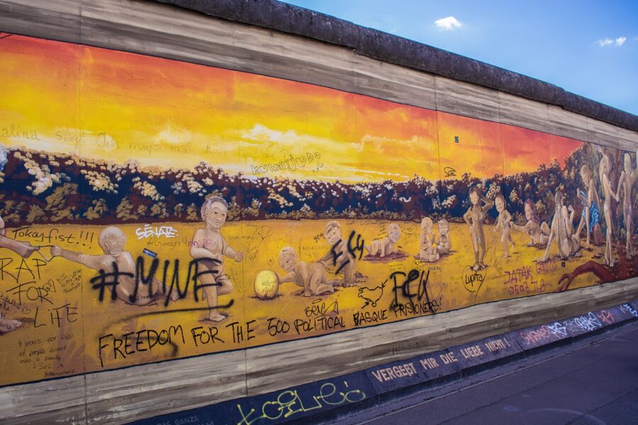 A section of the Berlin Wall in Germany, covered in colourful graffiti and street art, with a clear sky above.