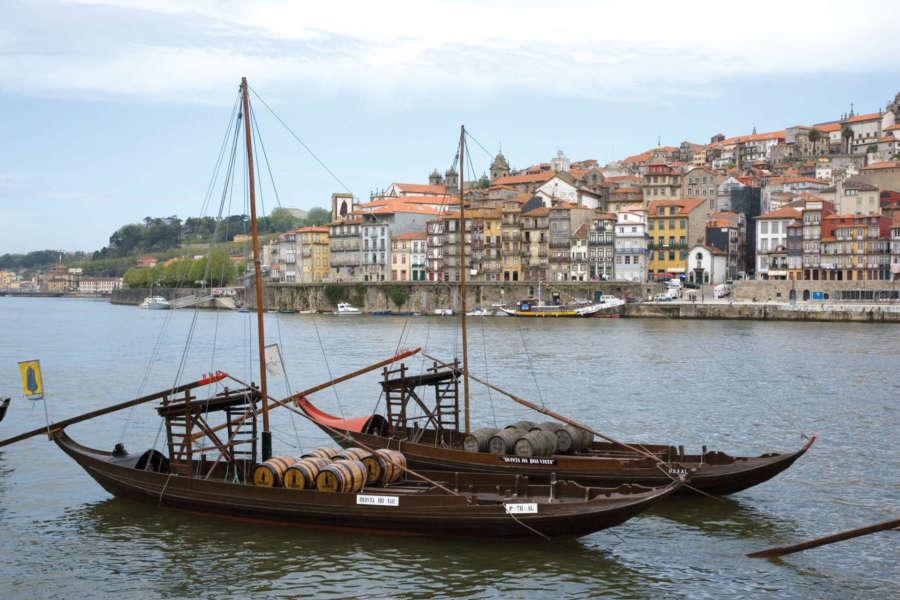 Traditional Rabelo boats docked on the Douro River in Porto, Portugal, with a picturesque cityscape of colorful buildings in the background. Porto wine tour, Travel Escapes Wine Tours
