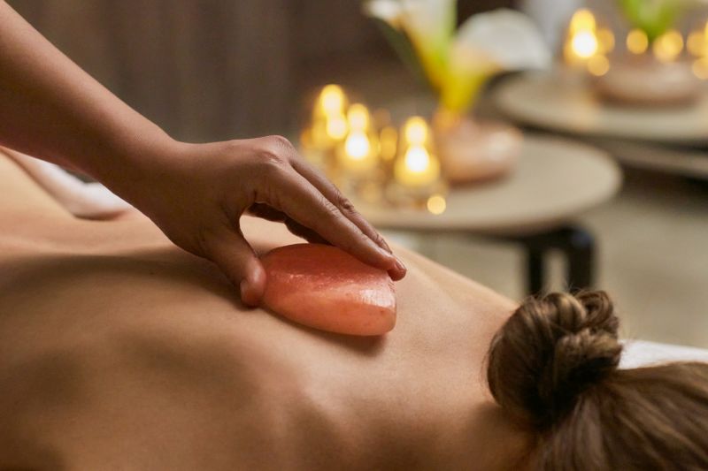 A woman relaxes during a soothing spa treatment on a luxury cruise ship, receiving a hot stone massage. Travel Escapes Explora Journeys