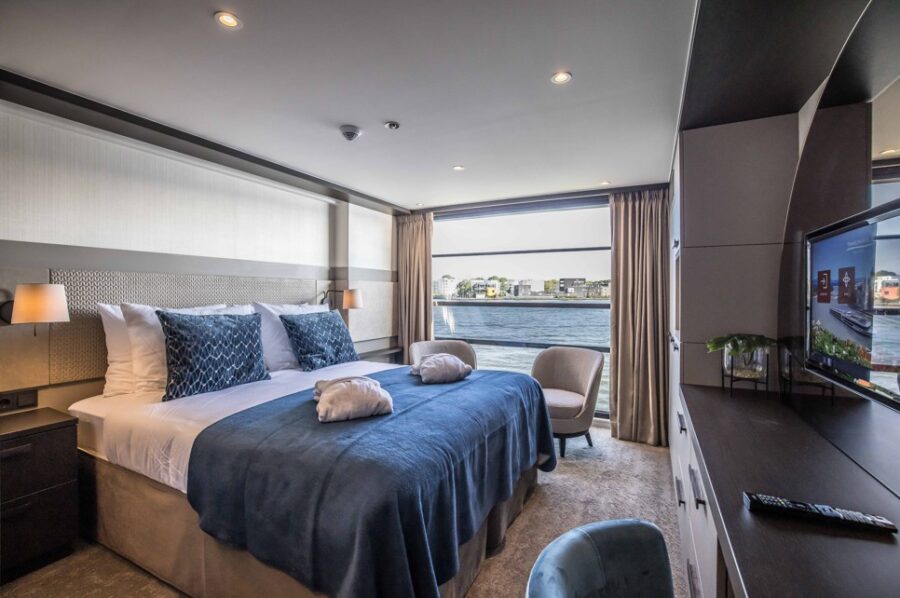 Elegant balcony cabin on the Travelmarvel Vega river cruise ship. A comfortable double bed with plush bedding faces a large window and balcony, offering scenic river views. Experience luxurious travel on your European river adventure.