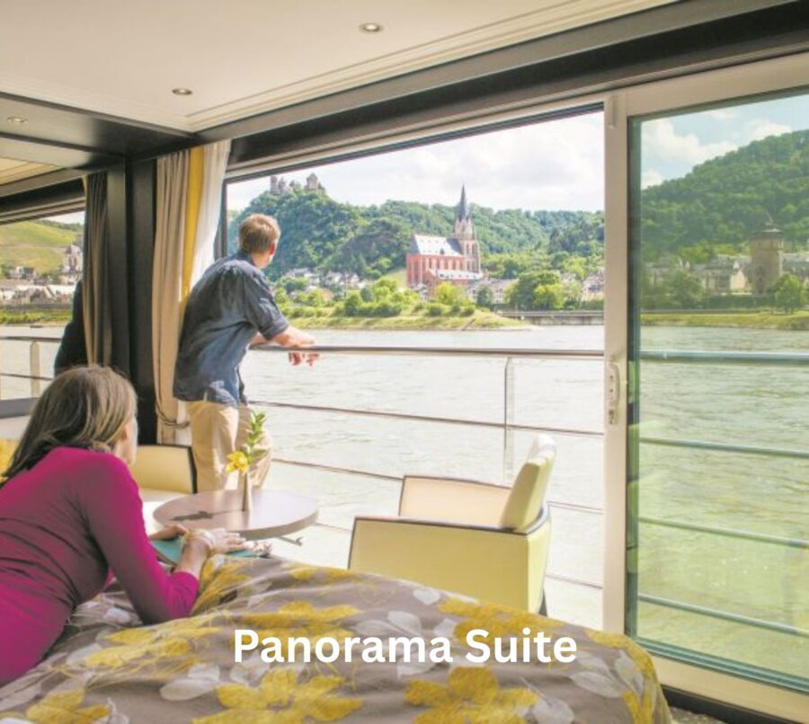 Panorama Suite on an Avalon river cruise, with a couple enjoying panoramic views of the Rhine River, including a historic castle and picturesque towns, from their spacious in-room balcony.