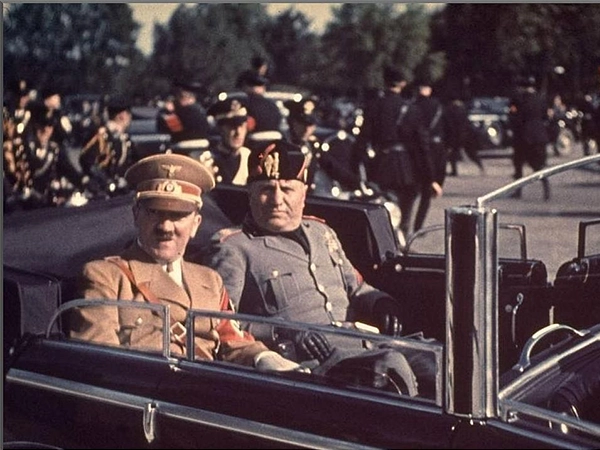 A historical colourised of a black and white photo of Adolf Hitler addressing a large Nazi rally.