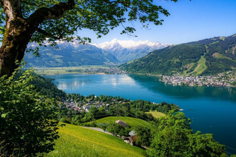 Stunning panoramic view of Zell am See in Austria, a crystal-clear lake surrounded by lush green hills and snow-capped mountains.