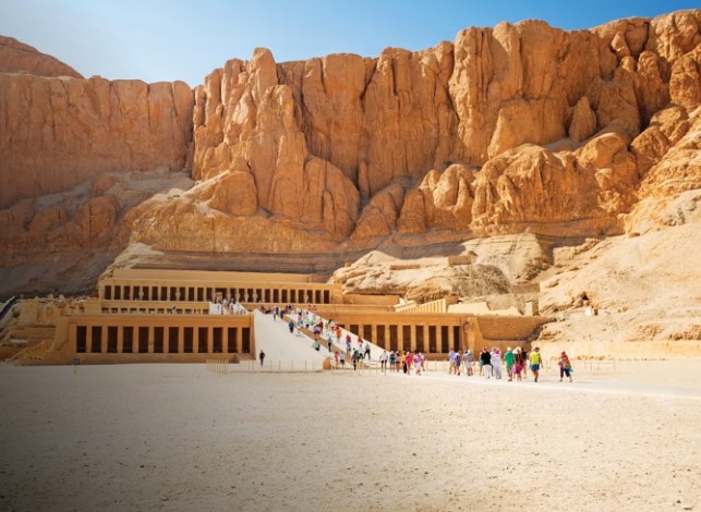 Terraced architecture of the Mortuary Temple of Hatshepsut, Luxor, Egypt. Tourists ascend the ramp against the backdrop of the Theban limestone cliffs.