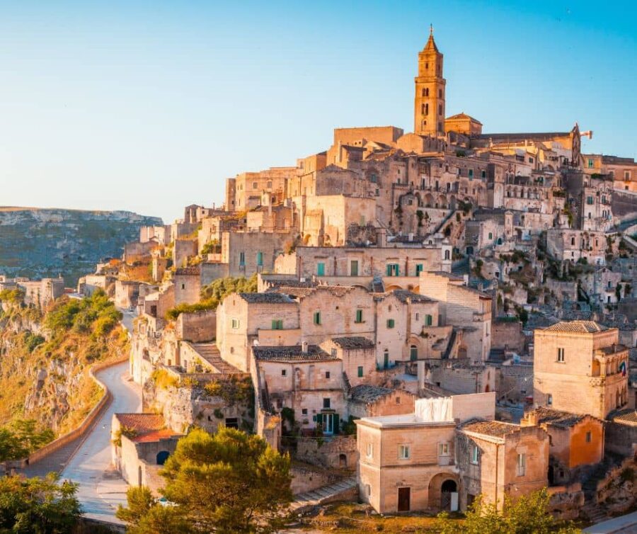 A stunning view of the ancient town of Matera, Italy, with its historic Sassi cave dwellings built into the hillside and a church tower rising above.
