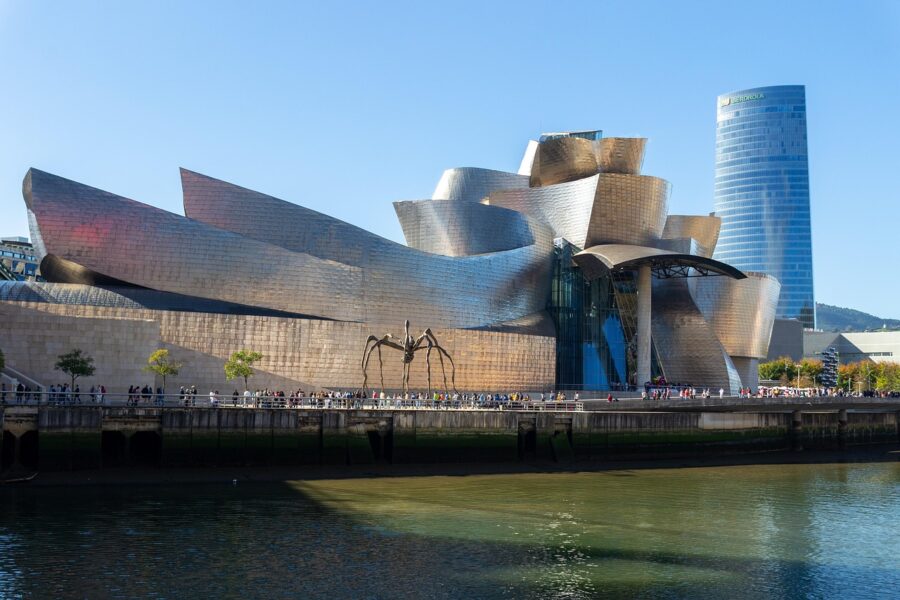 The glimmering titanium exterior of the Frank Gehry-designed Guggenheim Museum in Bilbao, featuring the large bronze spider sculpture 'Maman' on the waterfront.