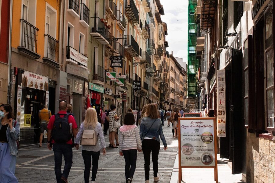 A vibrant street scene in Pamplona's Old Town, featuring colourful buildings with balconies and tourists walking along the paved pedestrian area.