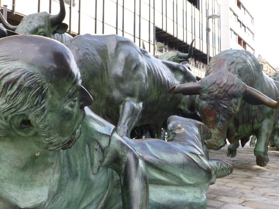 A detailed bronze sculpture depicting the chaos and energy of the Running of the Bulls, featuring runners falling and bulls charging through a cobbled street.
