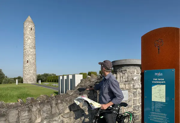 A visitor with a map looks toward the Irish Round Tower at the Island of Ireland Peace Park, a key stop on our WW1 battlefield tours from Ireland. Escorted battlefield tours from Ireland