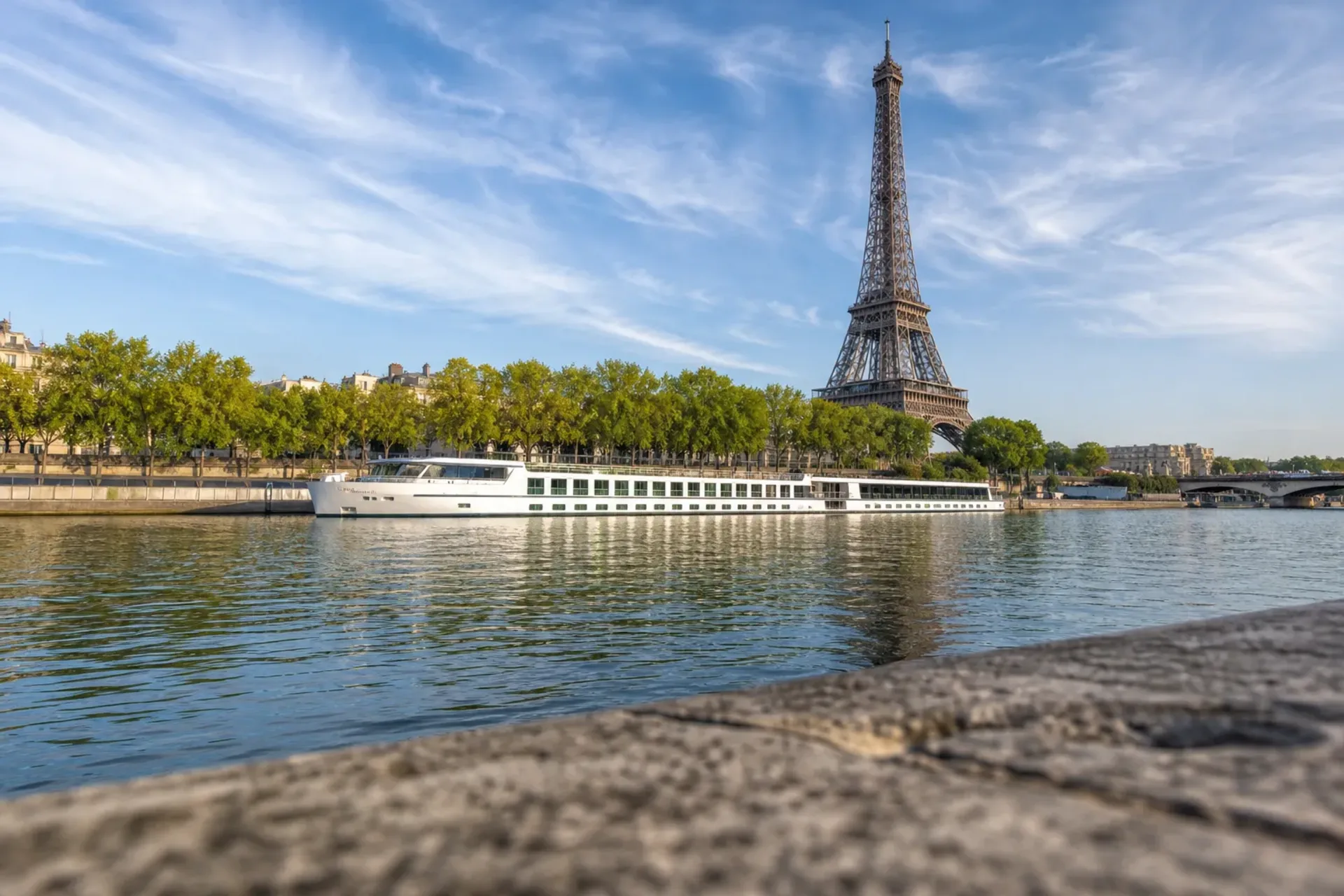 France-A river cruise ship docked on the Seine near the Eiffel Tower during a sunny Paris escape cruise.