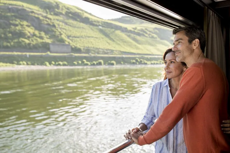 Couple admiring scenic river views from an Avalon Waterways Panorama Suite open balcony window
