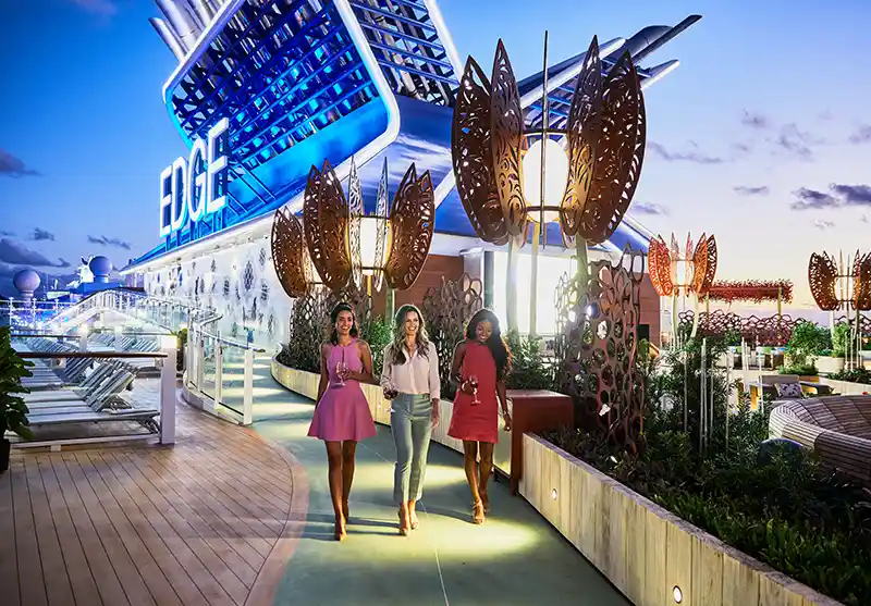 Three ladies strolling through the illuminated Rooftop Garden on board the Celebrity Edge cruise ship at night