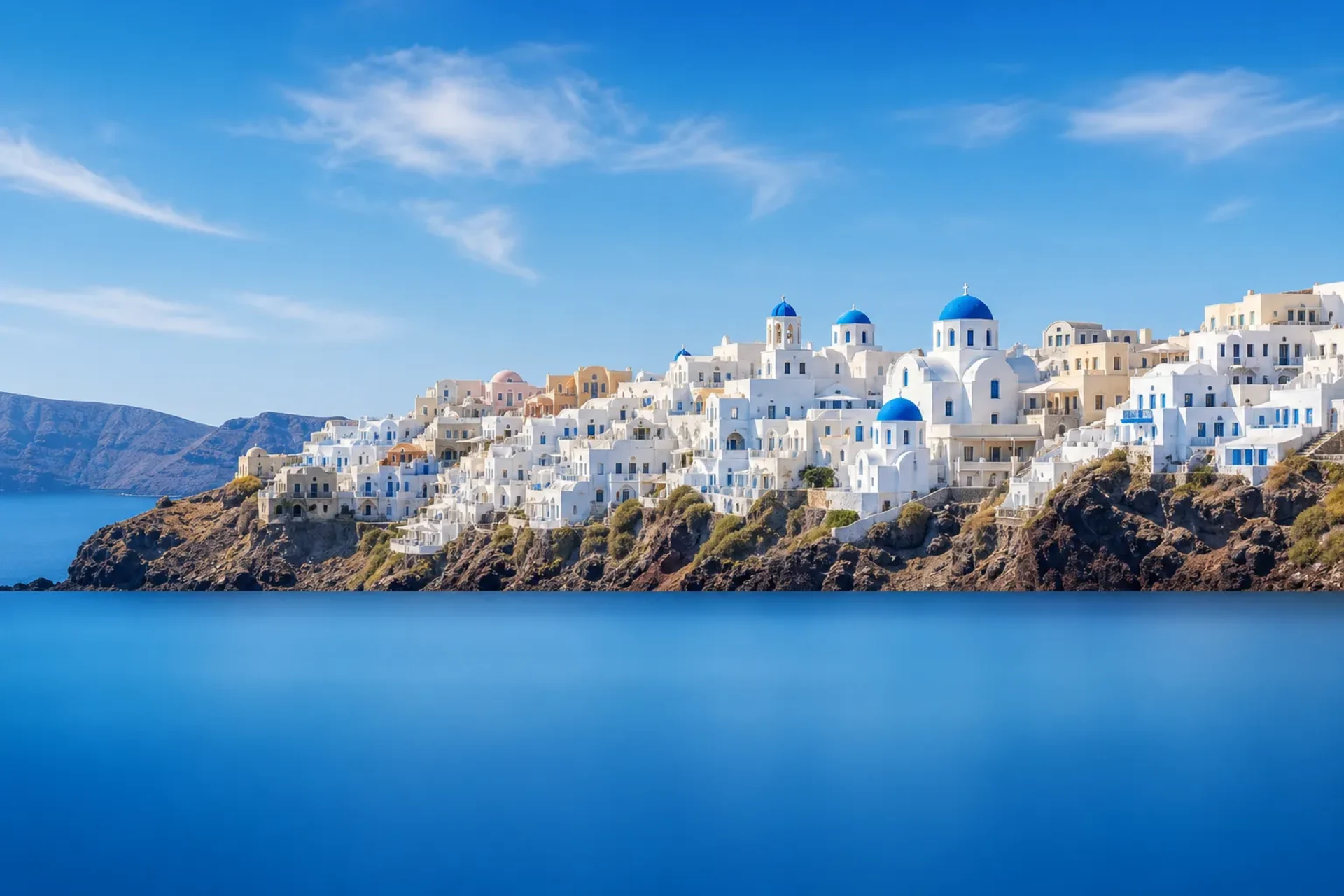 Italy, France, Greece-A sun-drenched panoramic view of Santorini's blue-domed churches and white buildings during an Italy France Greece cruise.