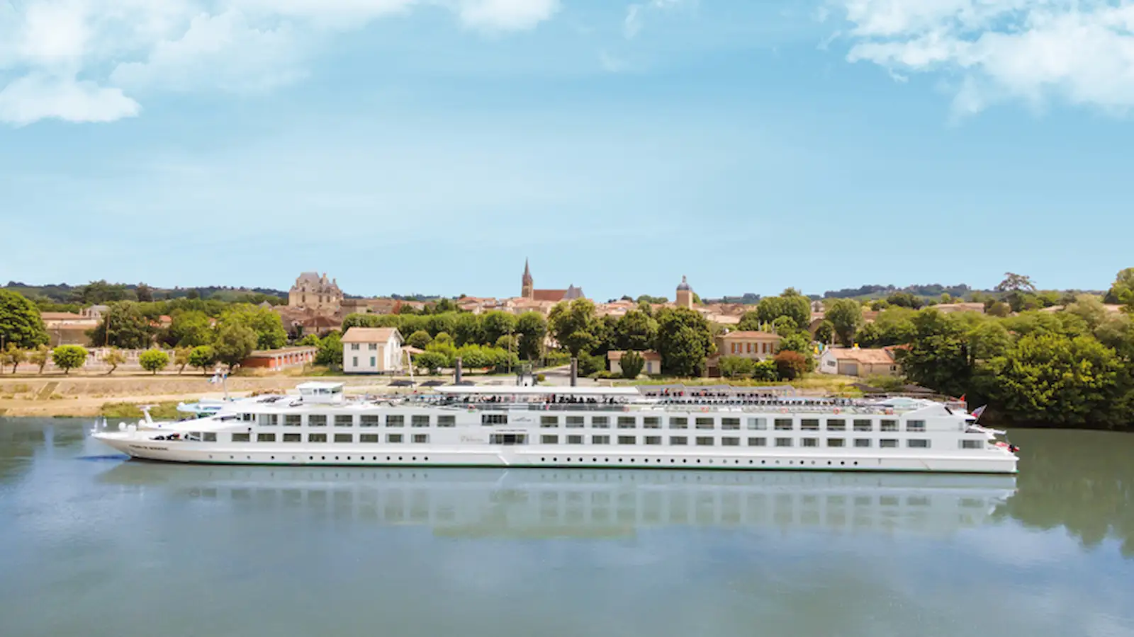 Luxury European river cruise ship sailing along a river past a historic countryside town