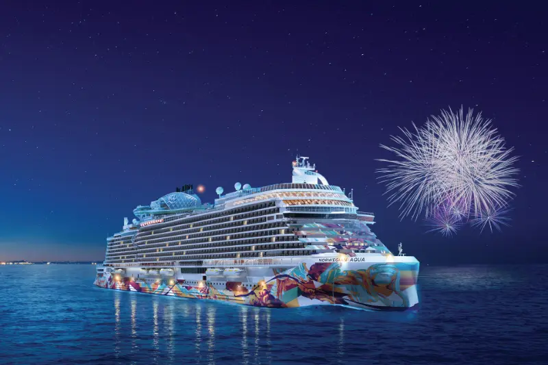 Norwegian Aqua cruise ship sailing on the sea at night with fireworks in the sky.