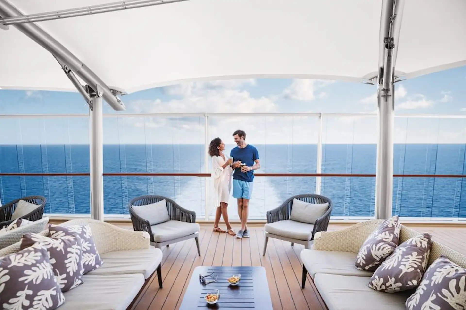 A couple enjoying drinks at the Spice H2O outdoor lounge on an NCL cruise ship with ocean views.