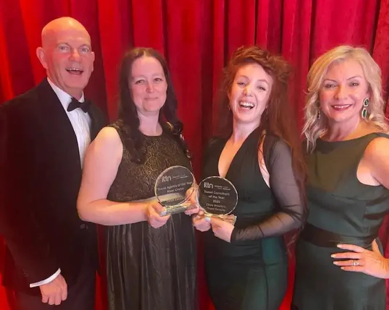 The Travel Escapes team (L-R: Alan, Eleanor, Chloe, and Celine) smiling together while holding their ITTN award trophies in front of a red curtain.